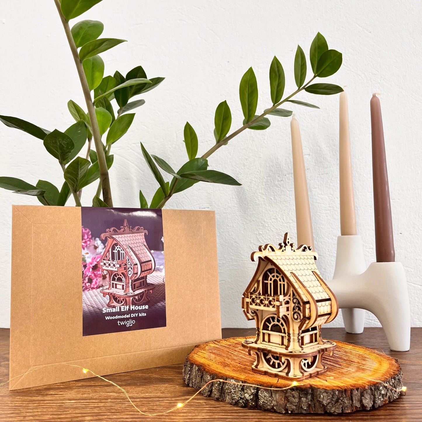 DIY kit packaging with garden house on a wooden surface with plants and candles in the background.