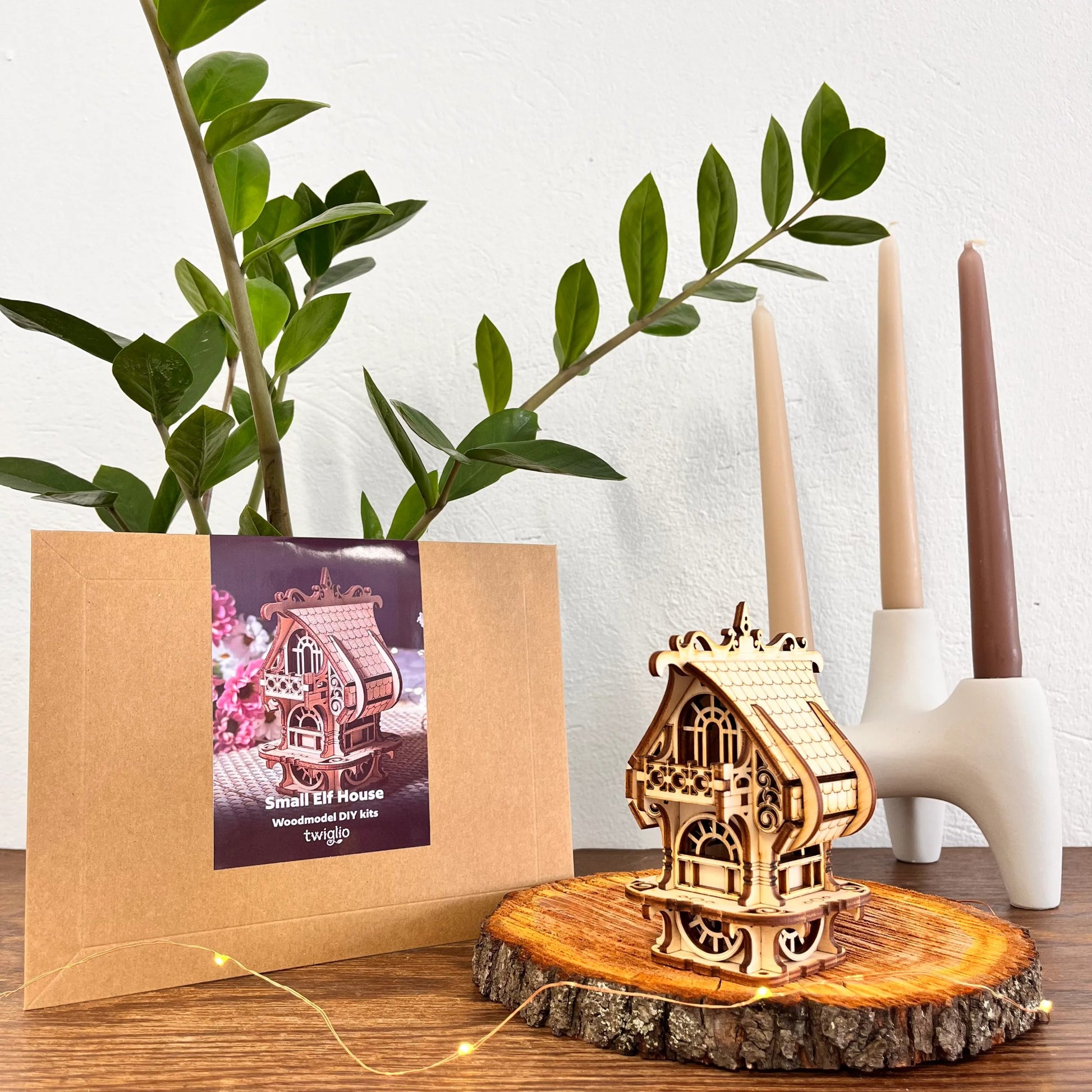 DIY kit packaging with garden house on a wooden surface with plants and candles in the background.