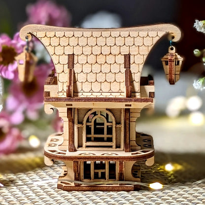 Wooden model of a house with a shingled roof on a textured surface with flowers in the background