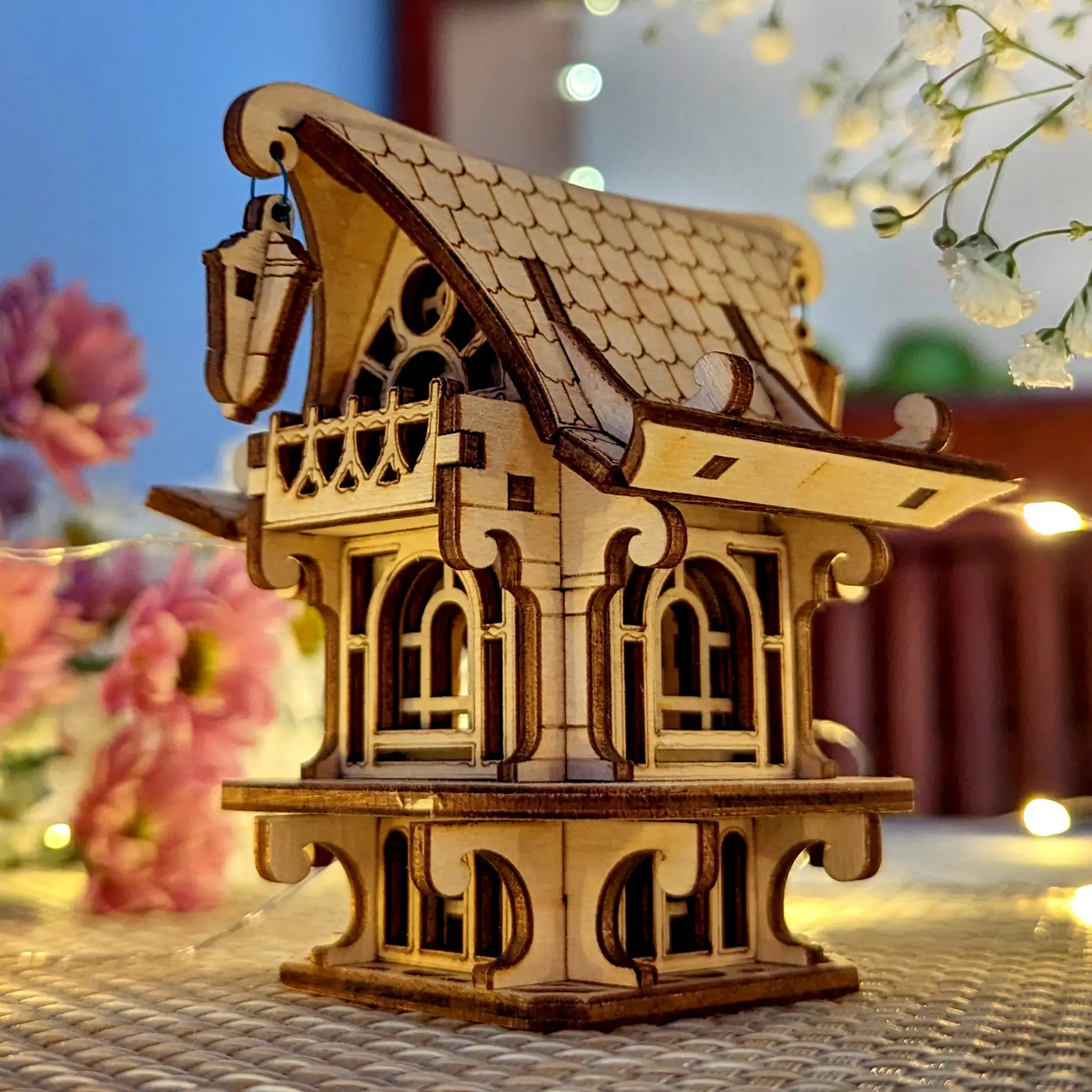 Wooden model of a house with decorative elements on a textured surface with flowers in the background