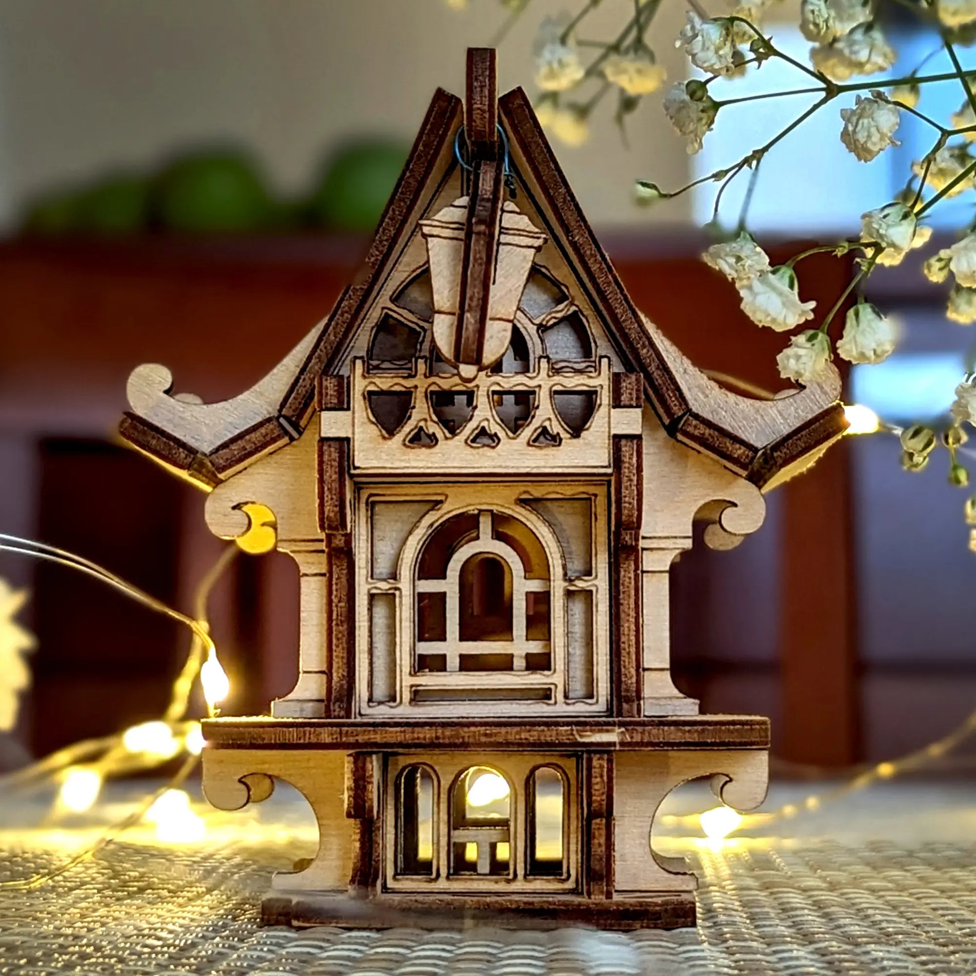 Wooden model of a house with decorative lights and flowers on a blurred background