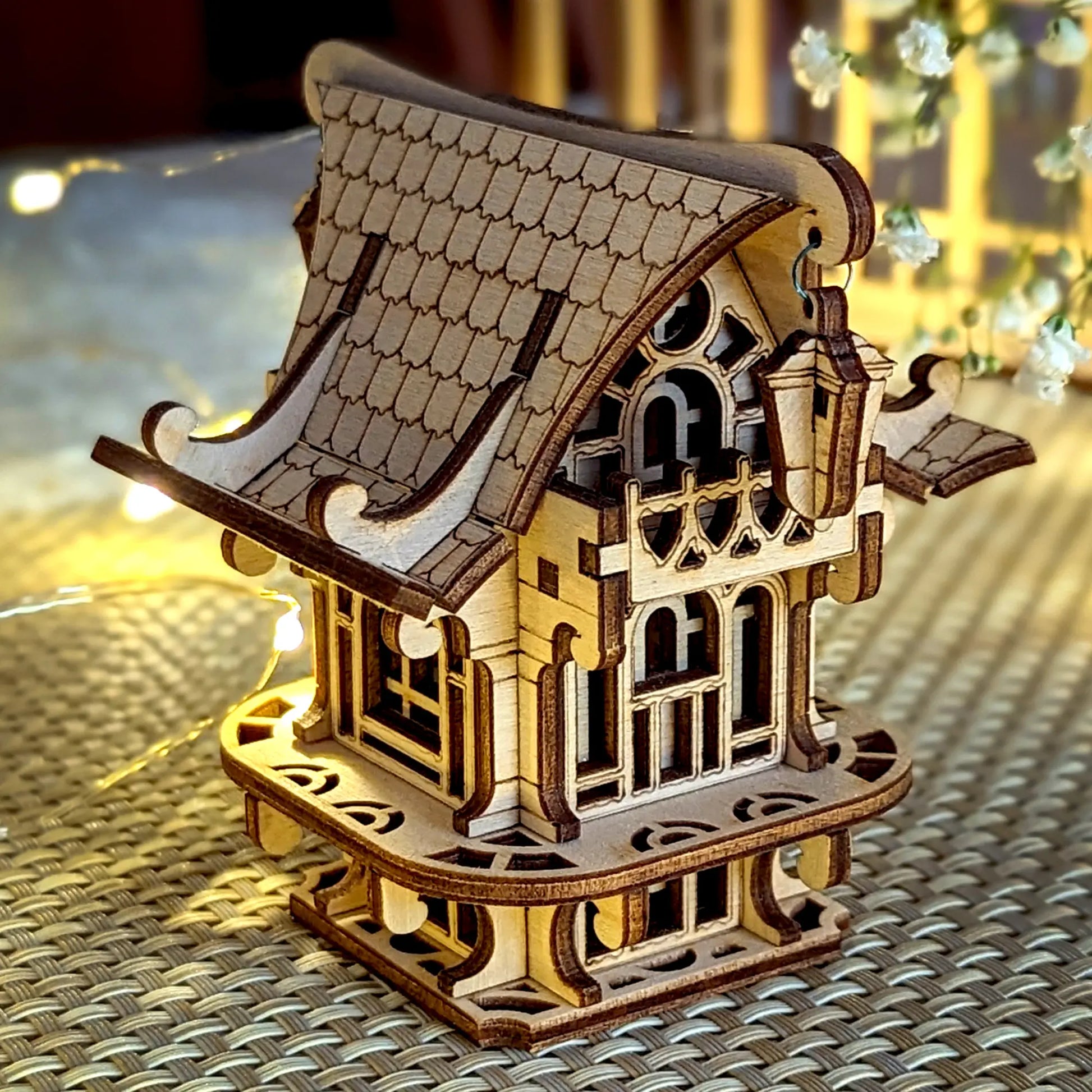 Wooden model of a house with a detailed roof on a textured surface with blurred lights in the background