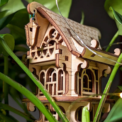 Wooden model of a house with intricate details, surrounded by green leaves.