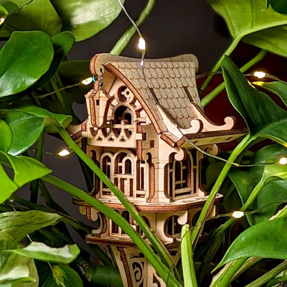 Wooden decorative house with string lights surrounded by green leaves