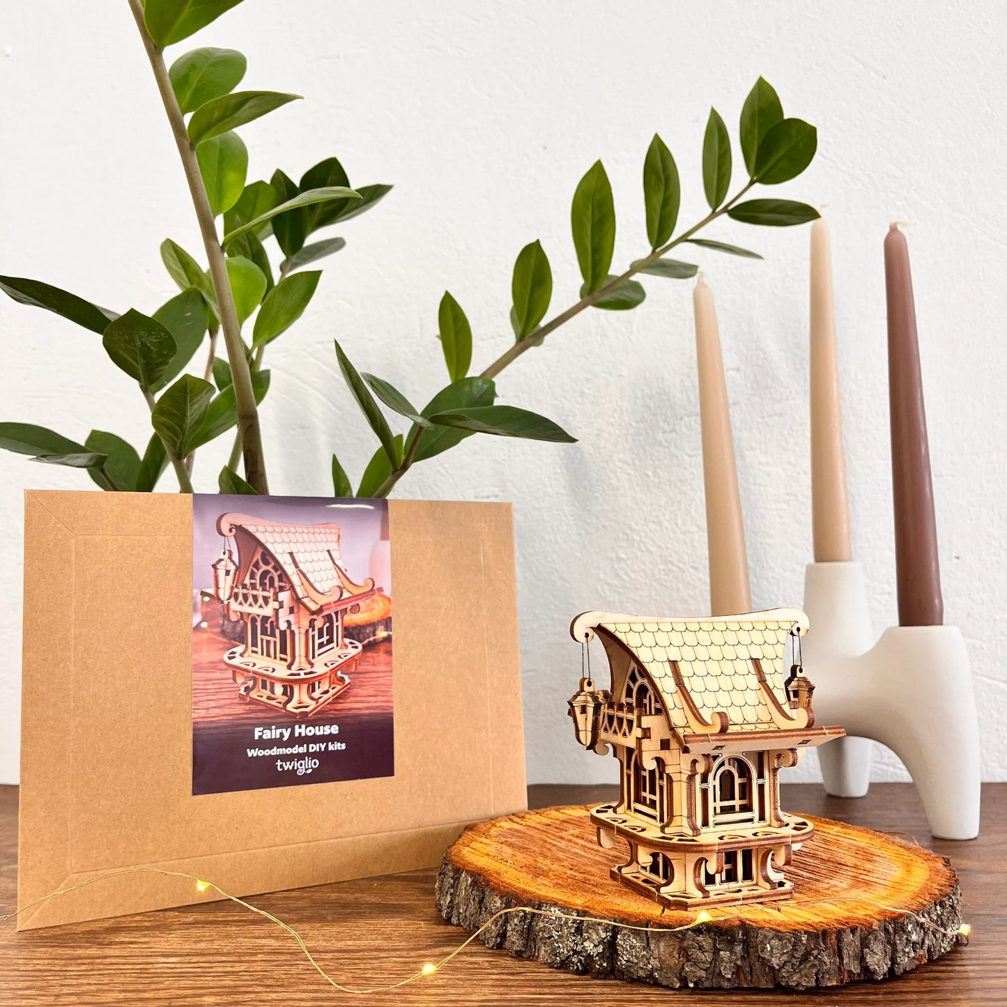 DIY kit packaging with garden house on a wooden surface with plants and candles in the background.