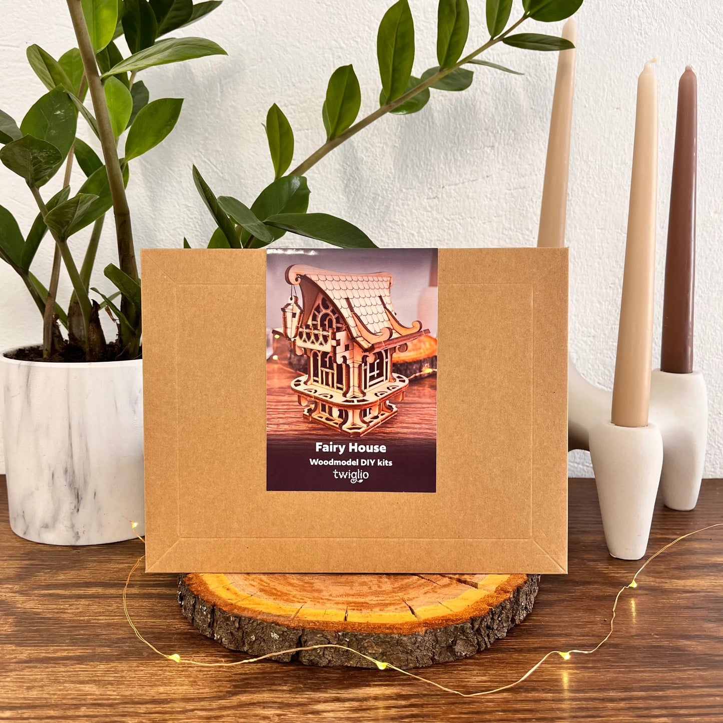 DIY kit packaging of garden house on a wooden surface with plants and candles in the background.