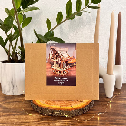 DIY kit packaging of garden house on a wooden surface with plants and candles in the background.