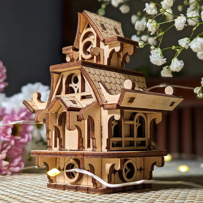 Wooden model of a house with intricate details on a table with flowers in the background