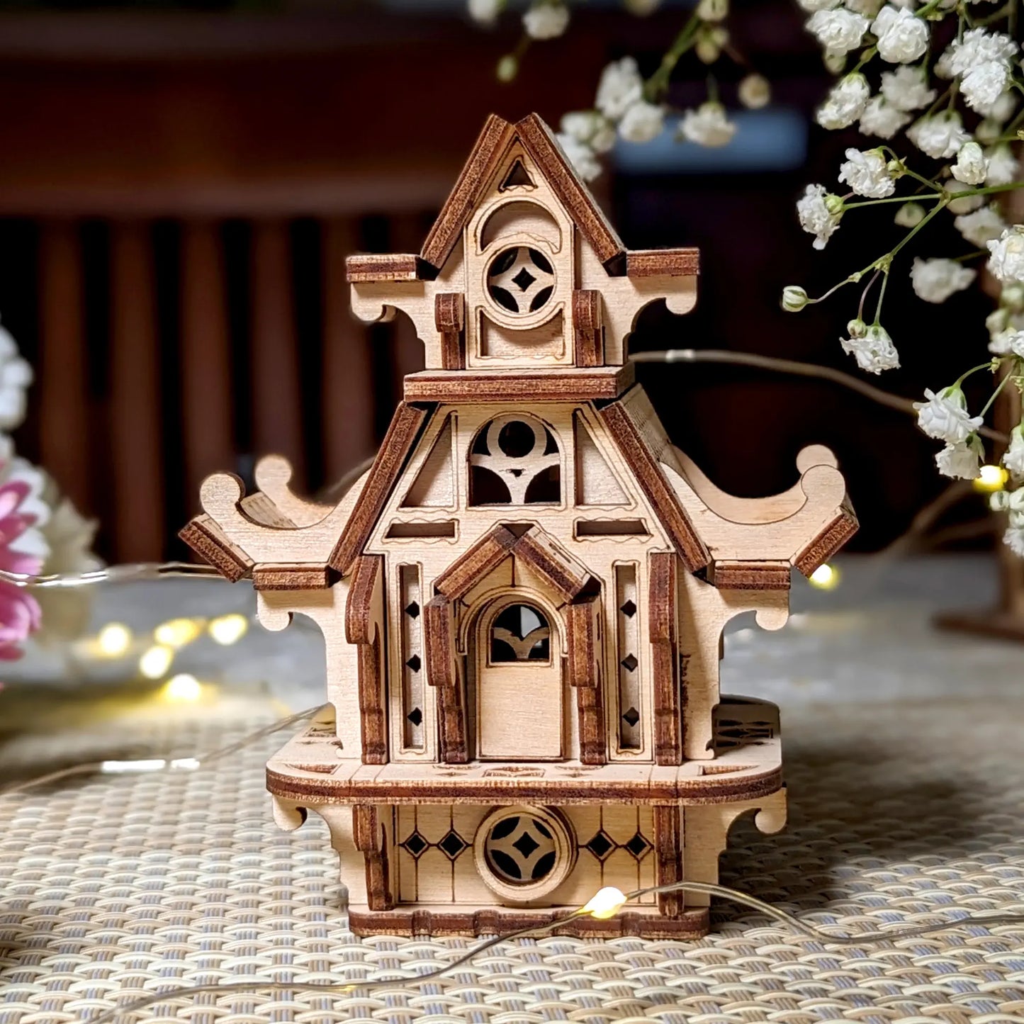 Wooden model of a decorative house with intricate details on a textured surface.