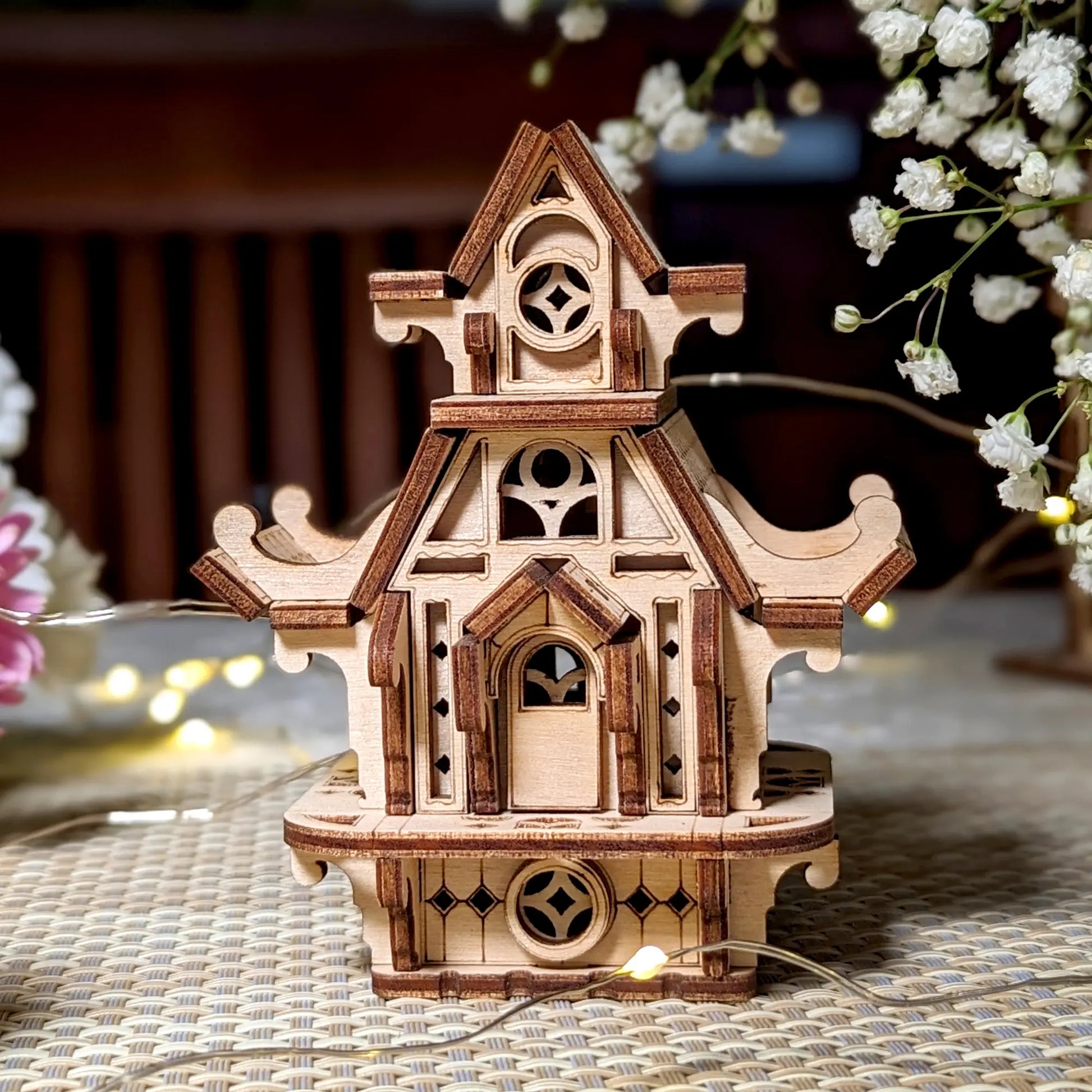 Wooden model of a decorative house with intricate details on a textured surface.