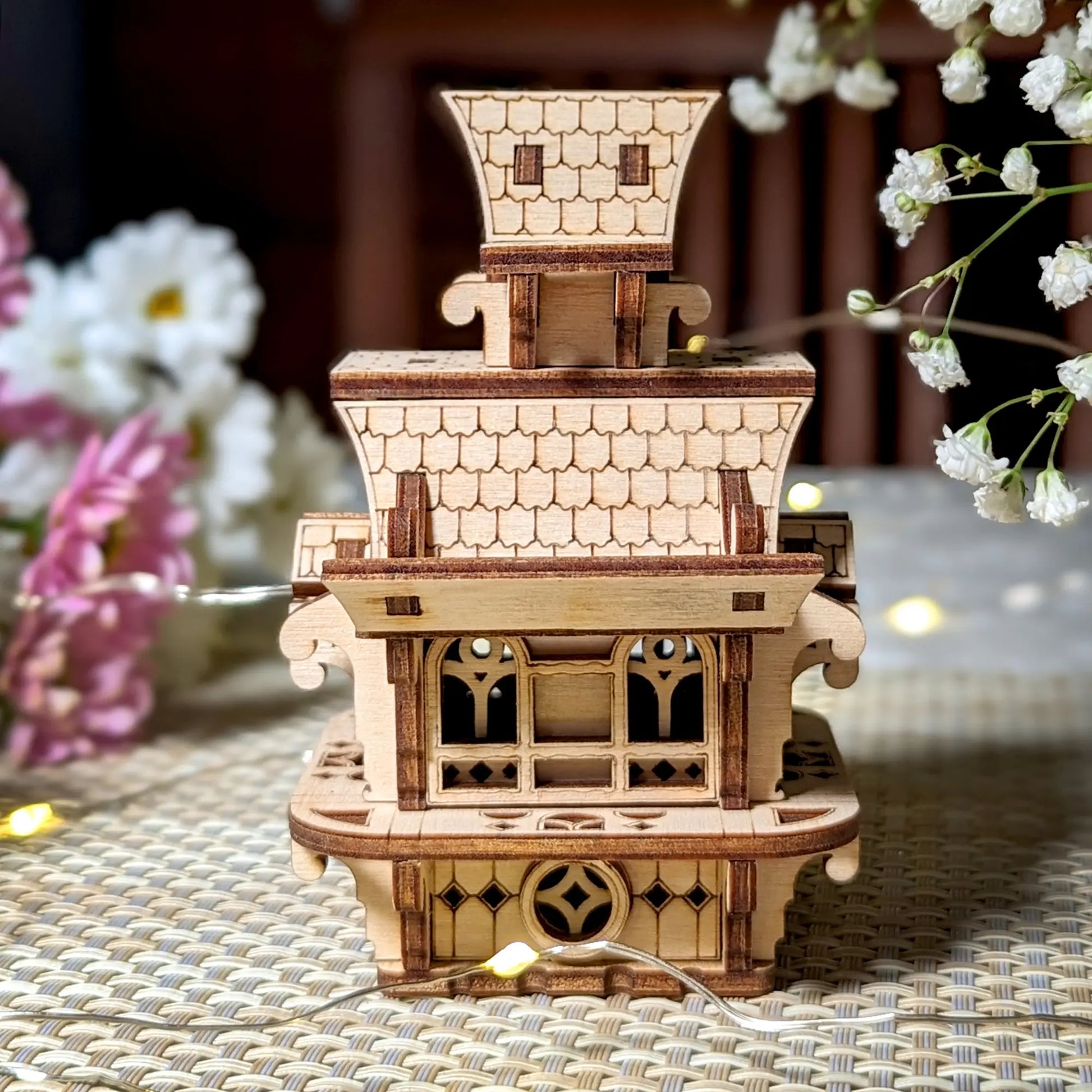 Wooden model of a pagoda with decorative elements on a woven surface.