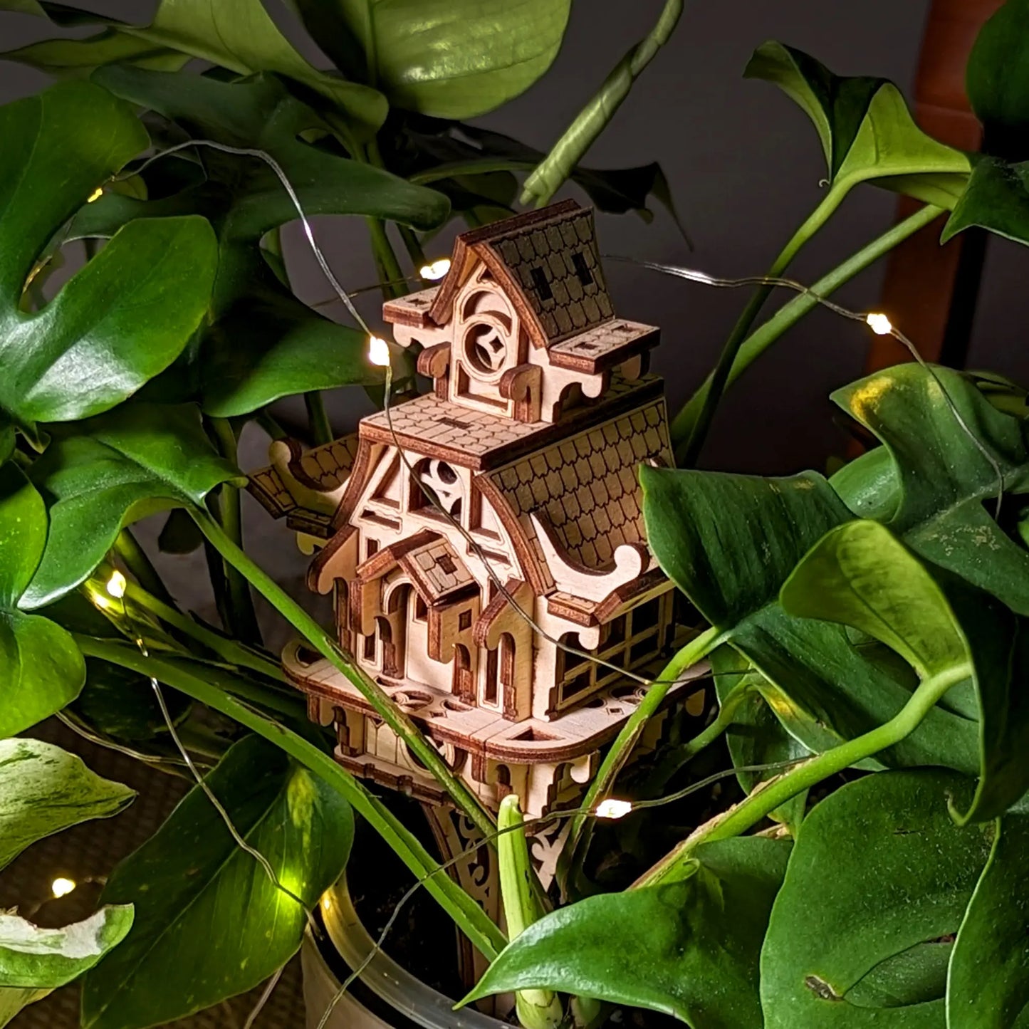 Wooden model of a house with string lights surrounded by green leaves