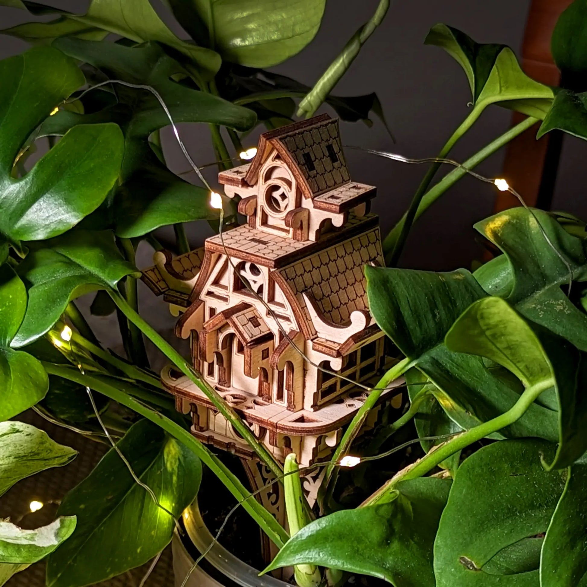 Wooden model of a house with string lights surrounded by green leaves
