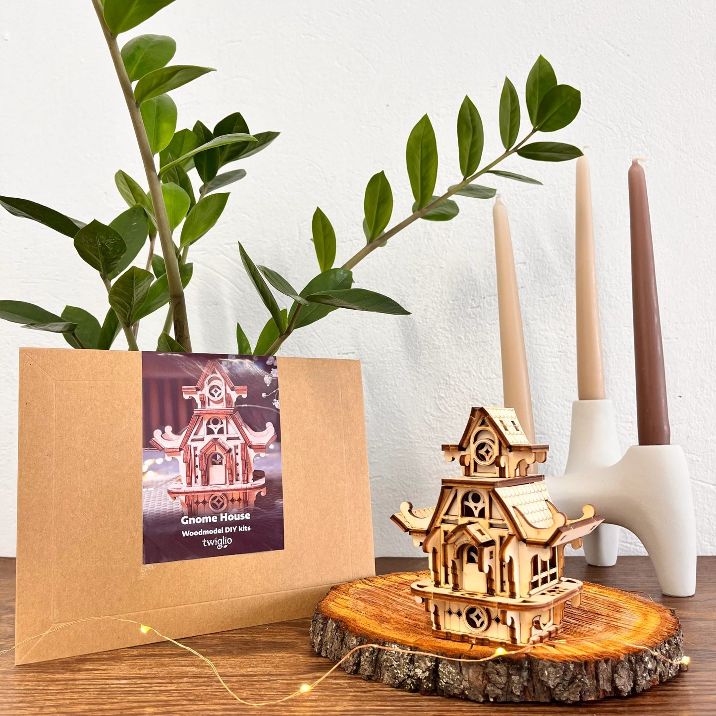 Wooden DIY kit packaging with garden gnome house on a wooden surface with plants and candles in the background.