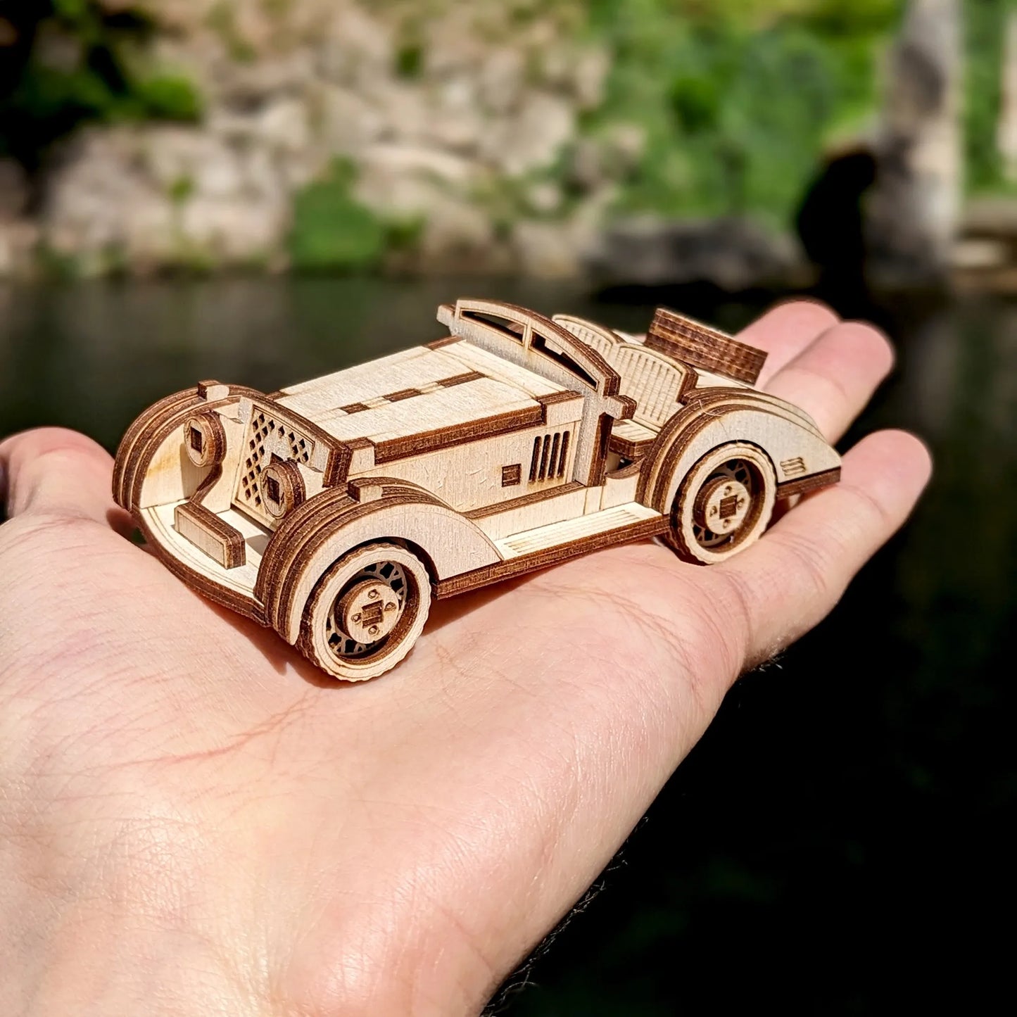 Small wooden vintage automobile miniature photographed on textured pavement with a natural background.