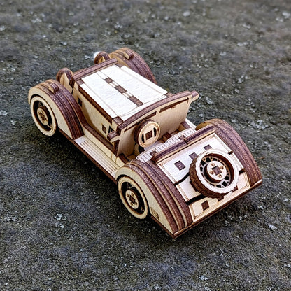 Vintage-style wooden sports car miniature made from laser-cut plywood, displayed on a rough outdoor surface.