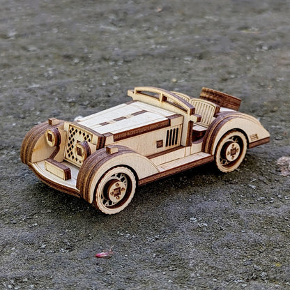 Vintage-style wooden sports car miniature made from laser-cut plywood, displayed on a rough outdoor surface.