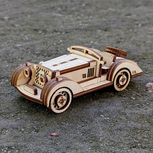 Vintage-style wooden sports car miniature made from laser-cut plywood, displayed on a rough outdoor surface.