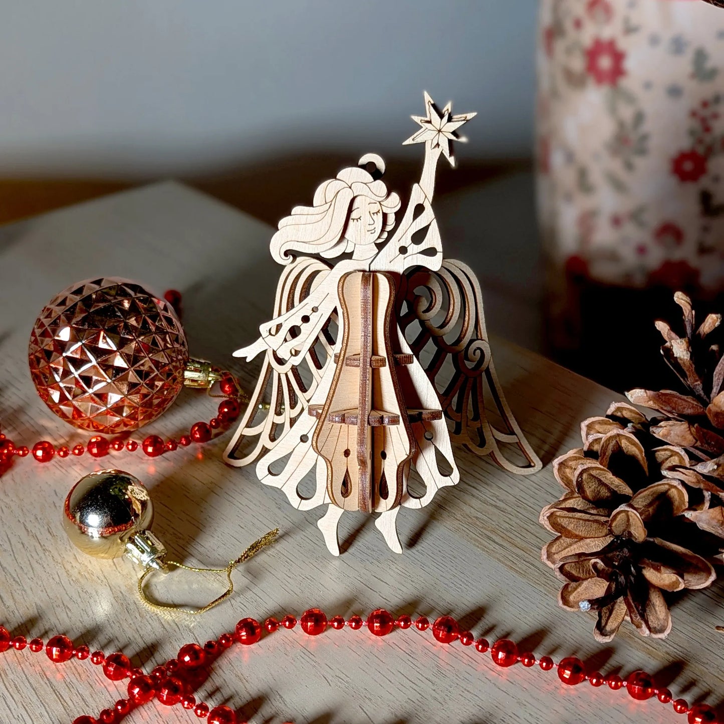 Wooden angel ornament with star on head surrounded by Christmas decorations on a wooden surface.