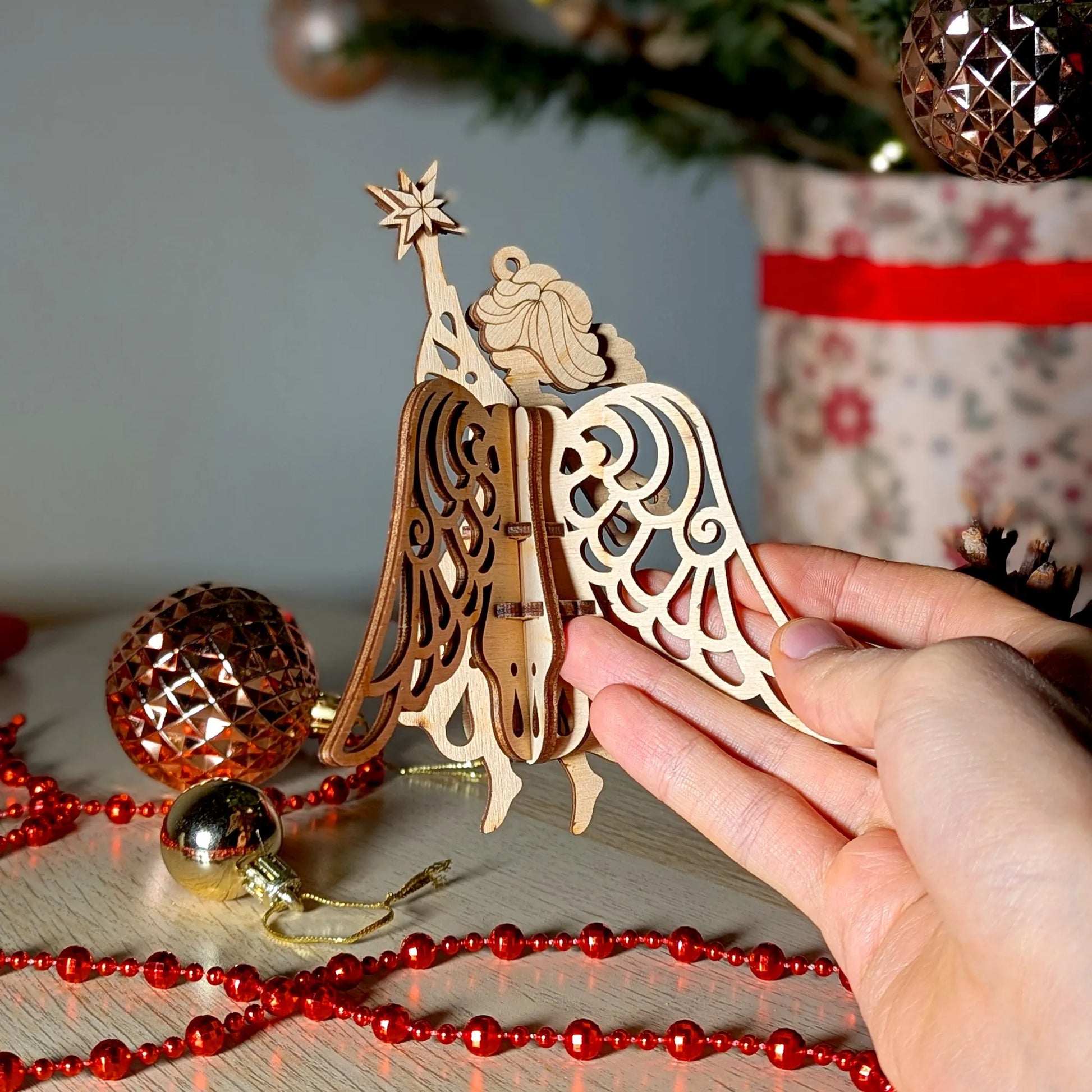 Wooden angel ornament held by a hand with Christmas decorations in the background