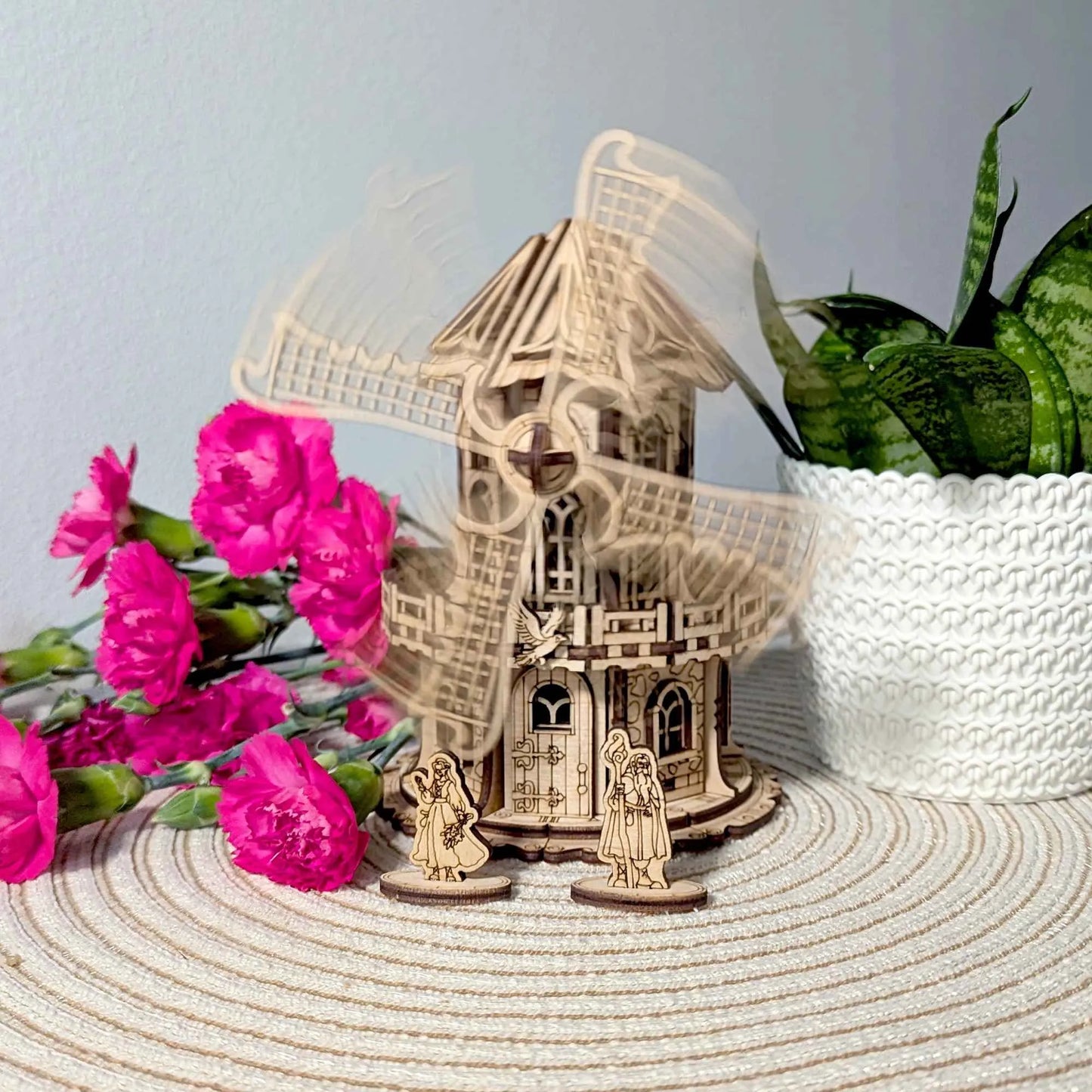 Handmade wooden windmill cottage with rotating blades and engraved fantasy-style accents, surrounded by vibrant flowers and greenery.