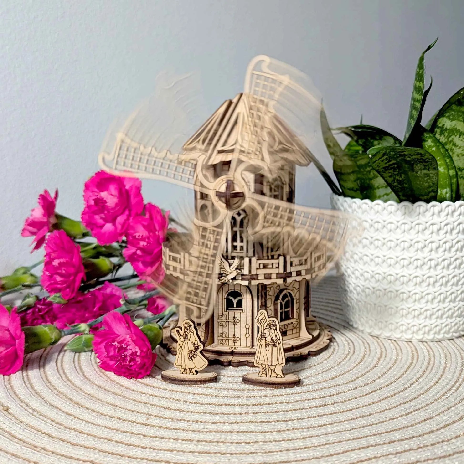Handmade wooden windmill cottage with rotating blades and engraved fantasy-style accents, surrounded by vibrant flowers and greenery.