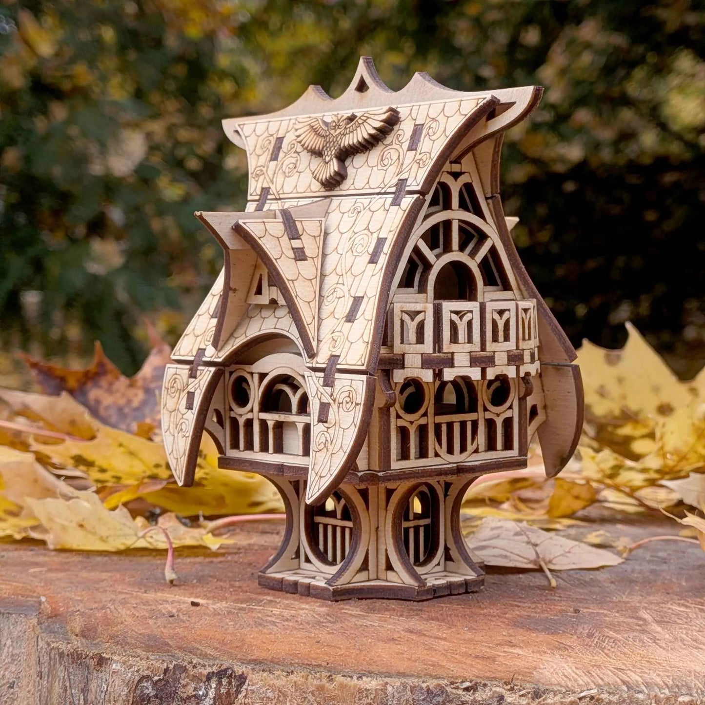 Miniature wooden fantasy house with a curved roof and carved windows, displayed among autumn leaves outdoors.