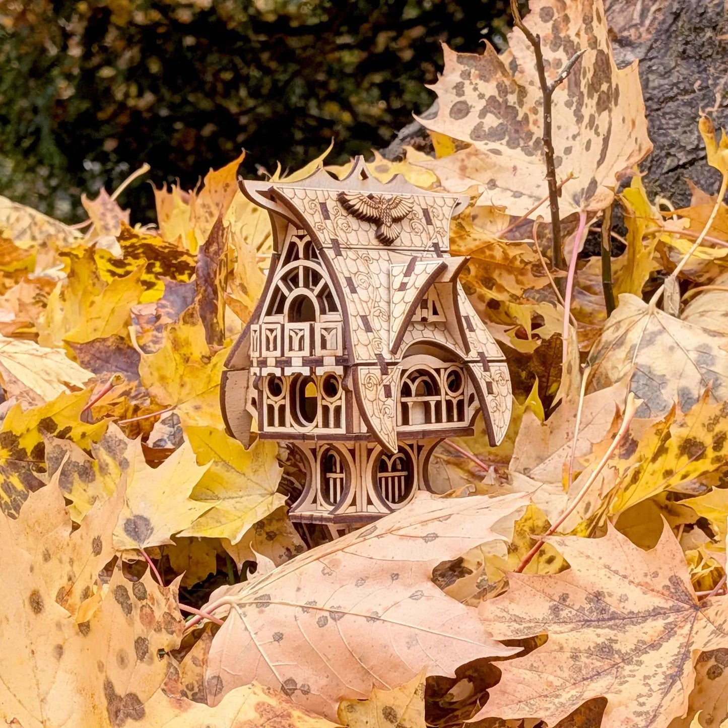 Detailed 3D plywood fairy-tale cottage with ornate roof patterns and gothic-style windows against a blurred fall background.