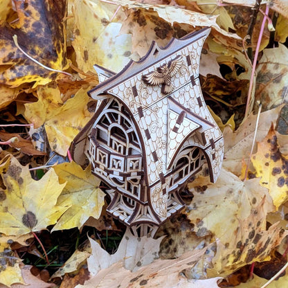 Miniature wooden fantasy house with a curved roof and carved windows, displayed among autumn leaves outdoors.