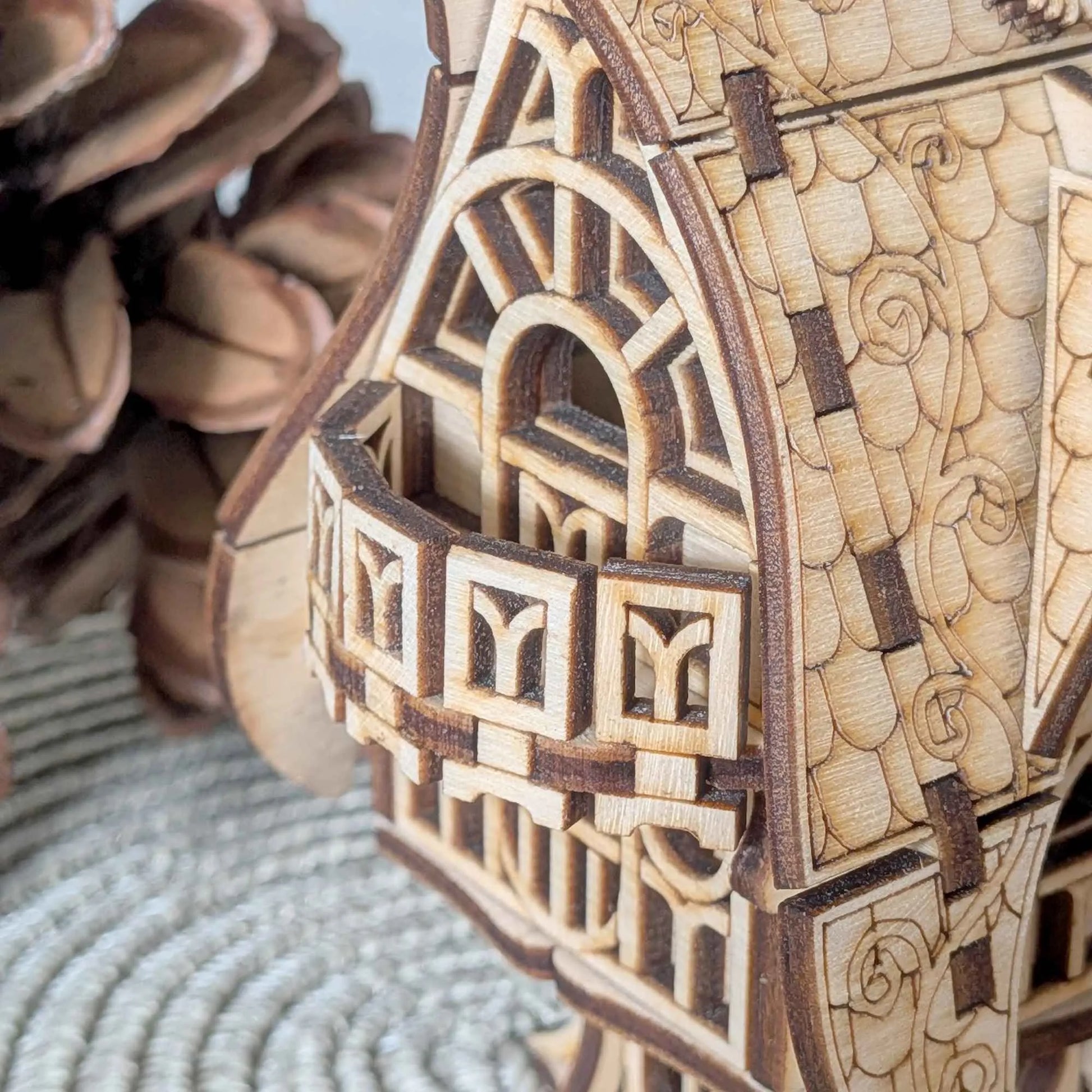 Handmade wooden fantasy cottage model with decorative roof details and arched windows, photographed in an autumn forest setting.