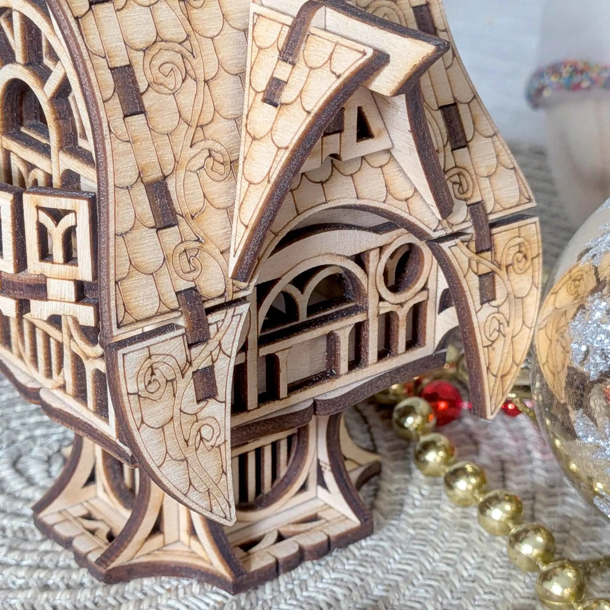 Detailed 3D plywood fairy-tale cottage with ornate roof patterns and gothic-style windows against a blurred fall background.