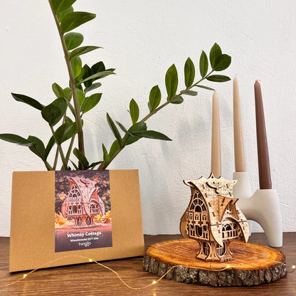 DIY kit packaging with garden cottage on a wooden surface with plants and candles in the background.