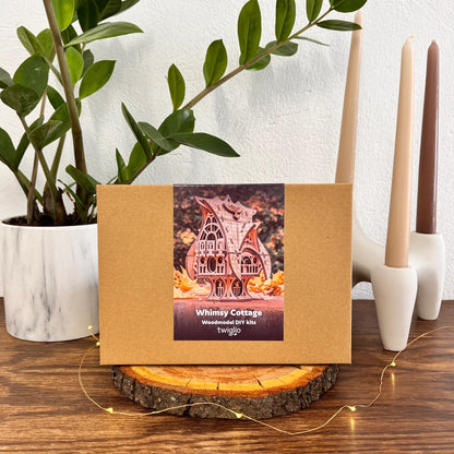 DIY kit packaging of garden cottage on a wooden surface with plants and candles in the background.
