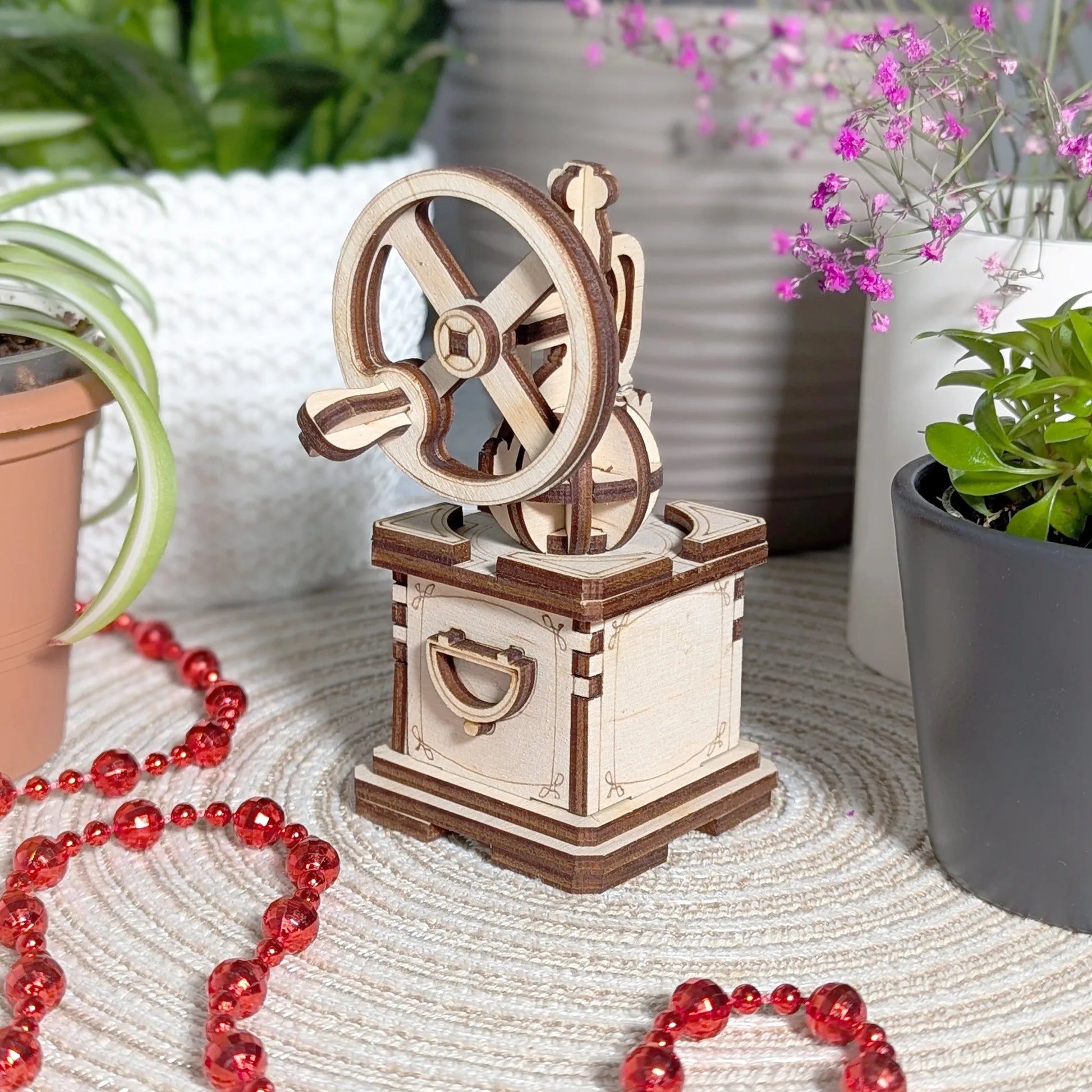 Wooden mechanical model on a textured surface with plants and beads in the background