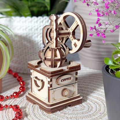 Wooden coffee grinder model on a textured surface with plants and beads in the background