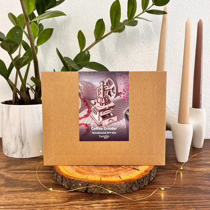 Kraft paper box with a coffee grinder model kit on a wooden surface with candles and a plant in the background.